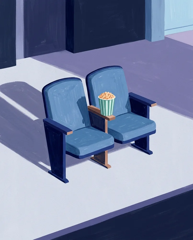 Two folding cinema seats face the dark auditorium, with a tub of popcorn between them.